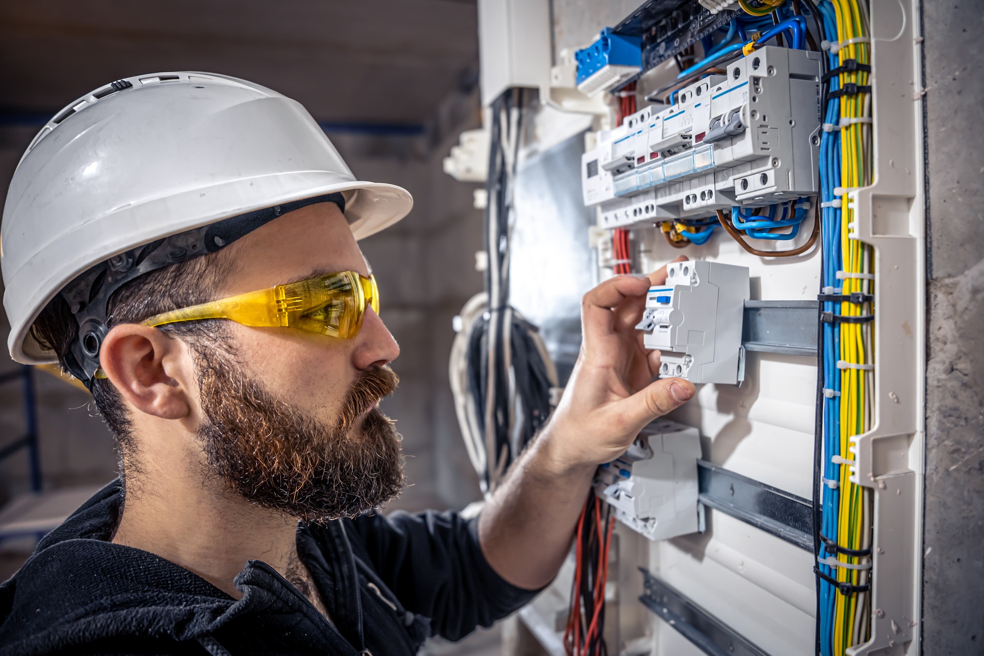 A male electrician works in a switchboard with an electrical connecting cable.