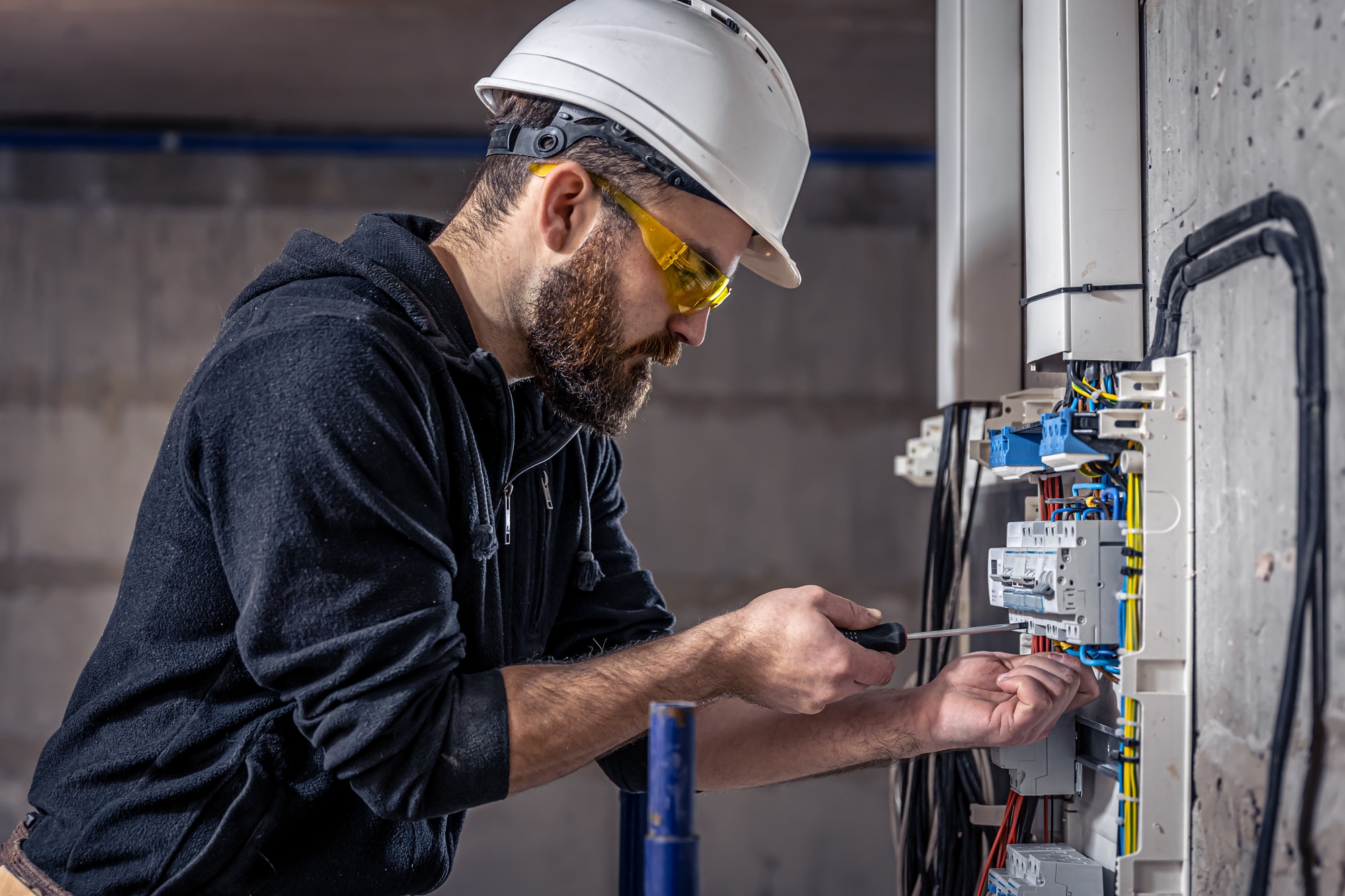 A male electrician works in a switchboard with an electrical connecting cable.